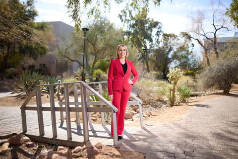 Stephanie Cooper in red dress suit standing outside near small wooden bridge