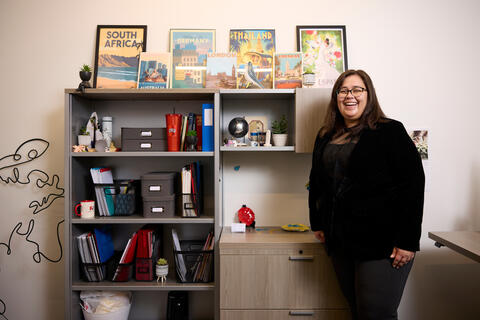 Kara Marinch stands next to a bookshelf that holds a collection of items from her travels