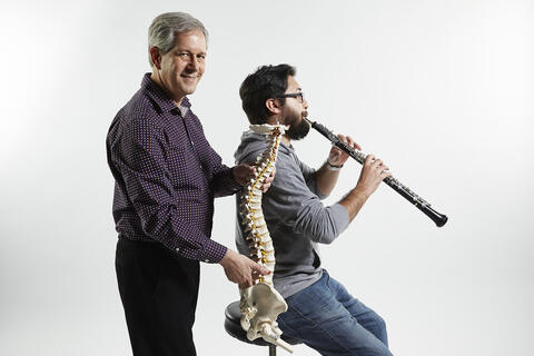 man holds replica spinal column to demonstrate seated musician's slouched posture