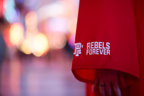 A closeup on the sleeve of a red UNLV graduation gown bearing the words "Rebels Forever"