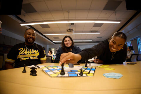 three students playing board game together