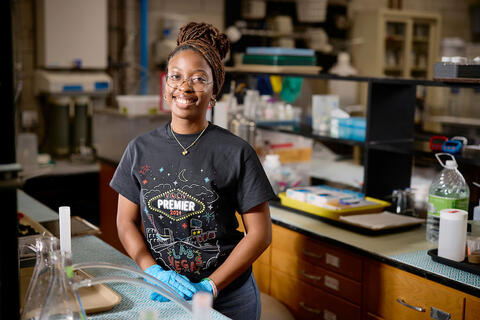 A woman wearing in a U-N-L-V Premier t-shirt while sitting down in a lab