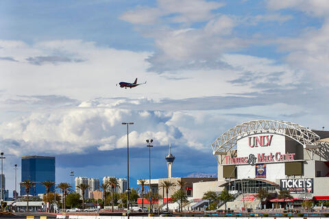An airplane flies over the Thomas &amp; Mack Center with the Las Vegas skyline visible in the background.