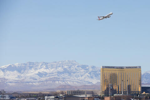 a plane flies over Las Vegas Strip with snowy mountains in background