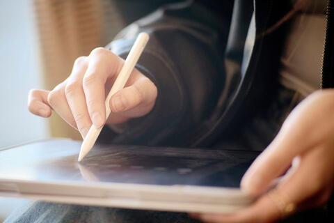A close-up of a person using a stylus on a tablet.