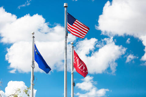 Three flags are flying against a blue sky with scattered clouds.