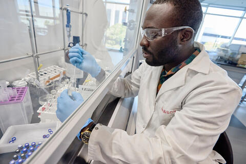 Gabson Baguma wears googles while working with lab equipment