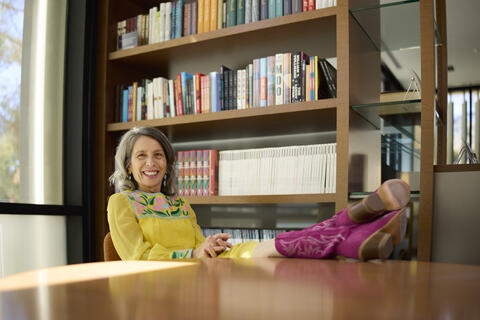 Colette LaBouff sits in front of bookshelf with her pink boots up on the table
