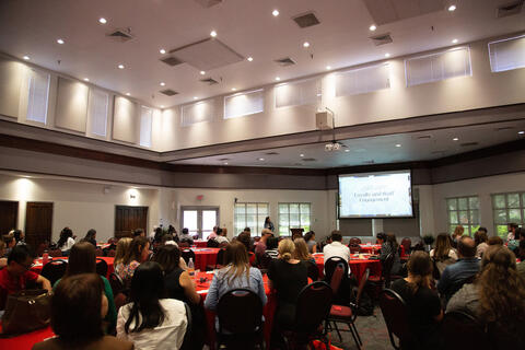 A room full people facing a large screen