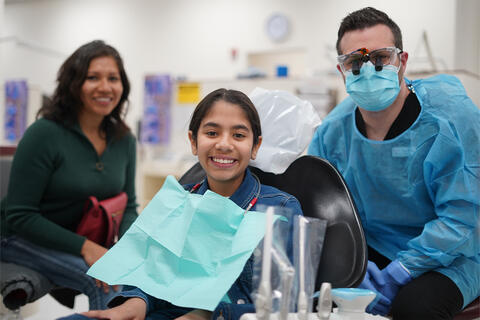 Dental student posing with a young patient and her mother