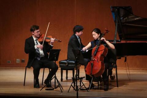 three musicians on stage performing on piano, violin, and cello