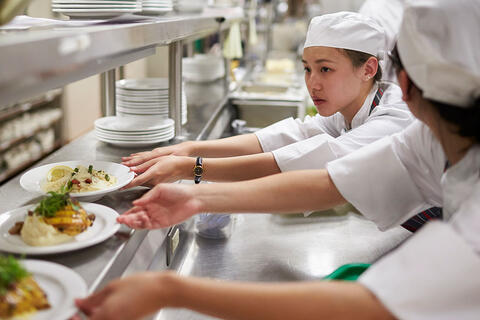 Two chefs grabbing plates of food from a shelf