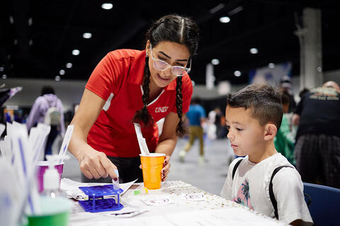 A woman is guiding a child through an experiment using science equipment on the table.