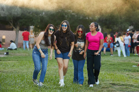 Four college students laughing and walking together across a grassy field