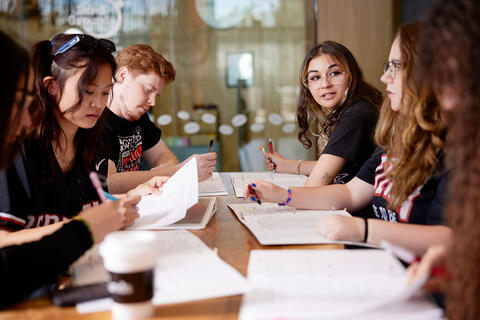 A group of people sitting at a table while writing down notes.