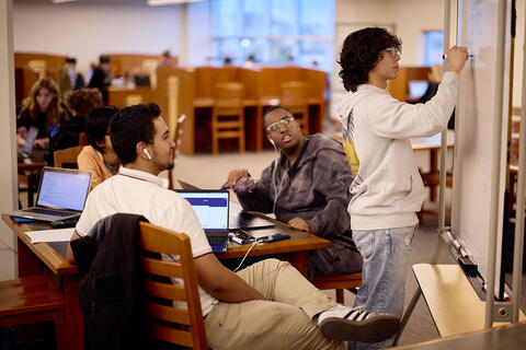 A man writing on a white board in front of a study group.