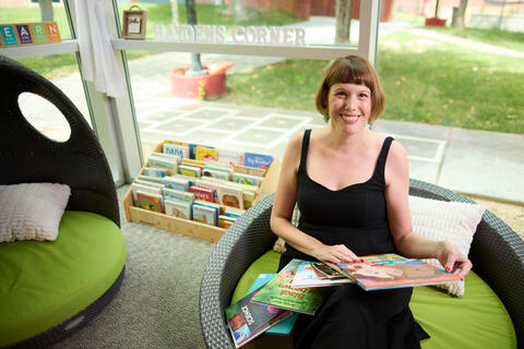 woman seated on round chair in preschool classroom surrounded by children's books