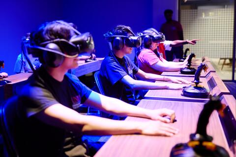 Two male and one female students sitting at desks wearing virtual reality headsets