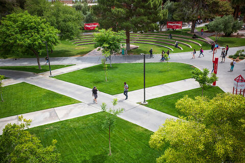Students walking across a intersecting concrete pathway surrounded by green lawns and trees.