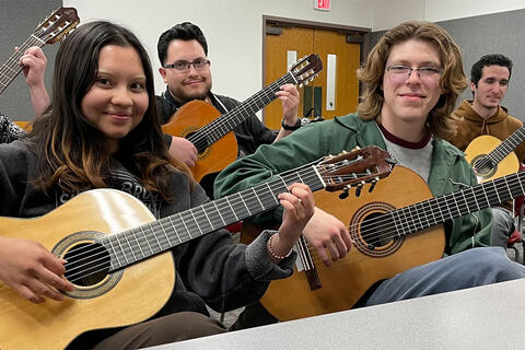 Four students holding up acoustic guitars