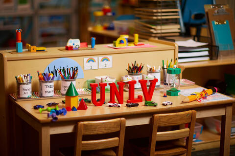 A classroom desk featuring organized art supplies, educational toys, and red 3D letters spelling “UNLV"