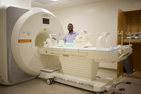 Ayan Sengupta stands next to MRI machine