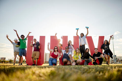 Group of students posing around the U.N.L.V. letters on a grass field