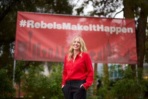 Karlie Passey in front of "Rebels Make It Happen" banner on campus