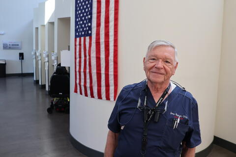 Dr. Raybeck stands near a U.S. flag while in his dental scrubs