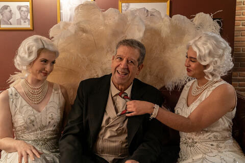 man sits between two women dressed like flappers