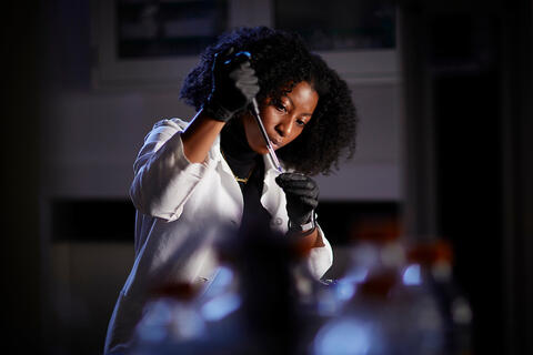 A scientist wearing a white lab coat and black gloves doing an experiment.