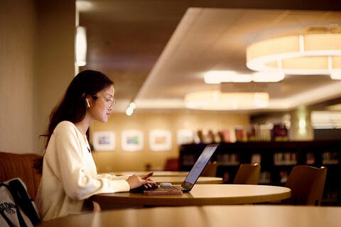 A person wearing earbuds and on their laptop