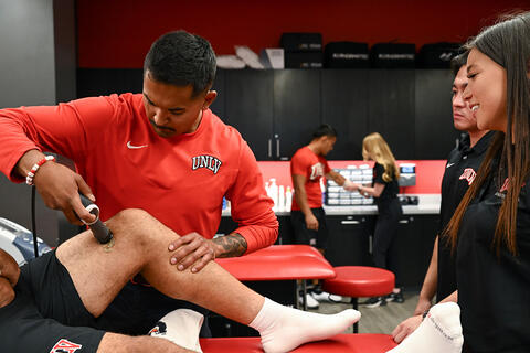 A trainer uses a handheld therapy device on an athlete’s thigh.
