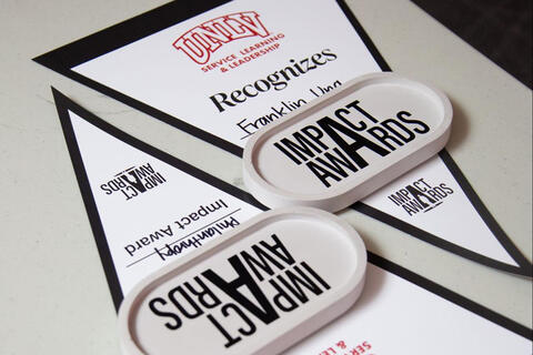 UNLV Service Learning & Leadership recognition certificates with two ‘Impact Awards’ plaques displayed on a table.