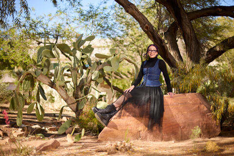 Ashley Lamb in a cool denim dress outfit on a rock next to an amazing cactus plant on campus