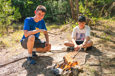2 students crouching over a campfire with sticks