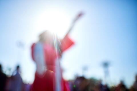 blurred image of a student wearing a red UNLV graduation gown throwing their cap into the air with their left hand
