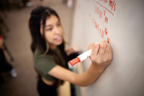 A student writing on a whiteboard using a red marker.