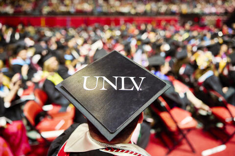 The top of a UNLV graduation cap overlooking a crowd of graduation students at Commencement.