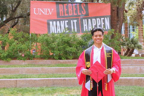 James Sarmiento wearing UNLV commencement robe in front of Rebels Make It Happen sign