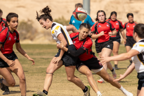 A group of rugby players with a player tackling an opponent in the center