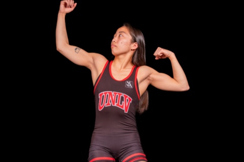 A woman in a U-N-L-V wrestling uniform striking a pose while looking at her arm