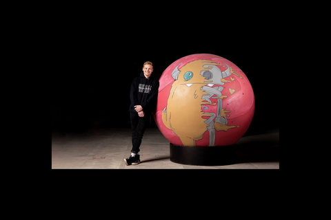 Ryan Brunty stands next to large globe with drawn character on it
