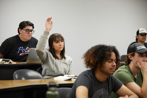 Students sit in a classroom as one student raises her hand during class