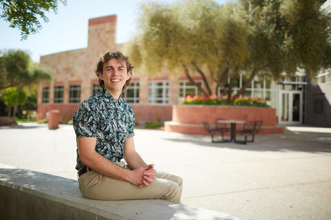 A student smiling while seated outdoors on campus