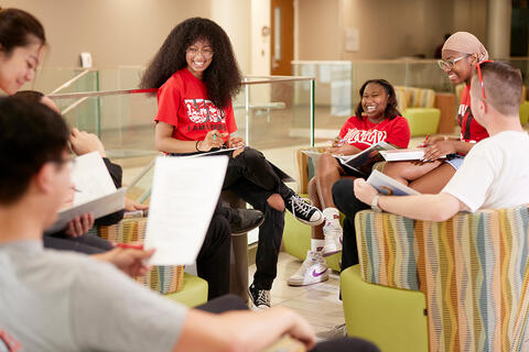 A group of students sits together in a lounge while holding notebooks and papers