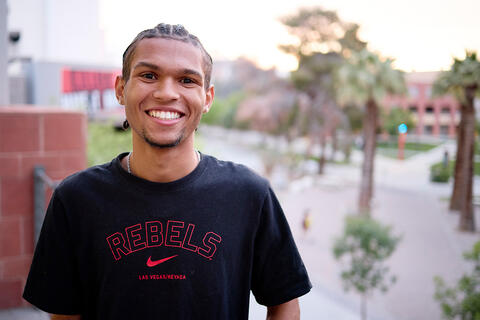 A smiling student wearing a black UNLV Rebels shirt stands outdoors on campus