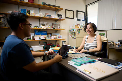Gloribert Roque-Melendez sits at a desk in her office talking to student