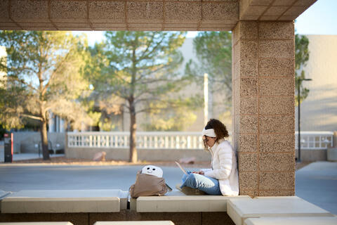 student sitting on bench using laptop
