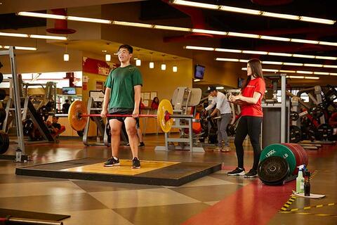Person doing deadlift with trainer on the side